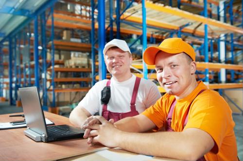 Two manufacturers in work room around desk with laptop. 