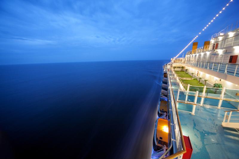 Top deck view of the side of a cruise ship at sea.